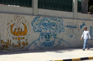 A Libyan man walks past graffiti of late Libyan leader Moamer Gaddafi is his hometown of Sirte on 13 October, 2012 (AFP).